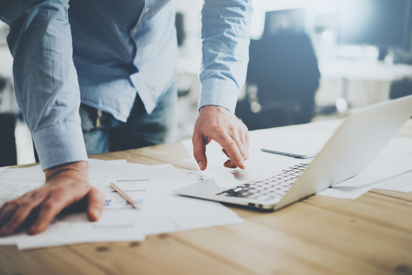 Businessman working in modern cretive studio. Using generic design laptop. Architectural project on table. Blurred background, horizontal mockup.